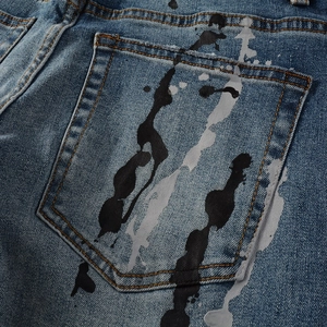 Dettaglio jeans blu con schizzi di vernice nera artistica e cuciture arancioni a contrasto