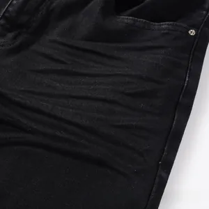Close-up detail of black denim jeans with vintage whiskered wash and metal rivet