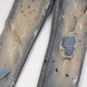Detail of distressed blue denim jeans featuring colorful paint splatters and ripped knees