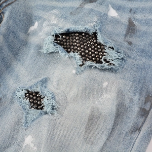 Detailed macro view of denim jeans with fringed holes and silver studs on black patches