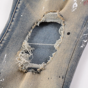 Detailed macro view of distressed denim fabric with paint splatters and frayed hole texture