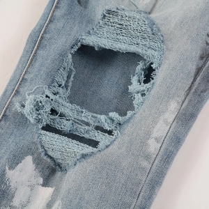 Close-up of distressed denim jeans featuring ripped knees and white paint splatter details