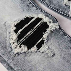 Close-up of distressed denim jeans with ripped holes and black ribbed fabric patches
