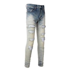 Dettaglio dei jeans slim da uomo azzurri con strappi consumati e toppe di strass lucidi