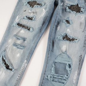 Close-up of light blue jeans featuring black rhinestones and white paint splatter