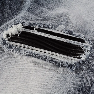 Detail of light blue washed denim with distressed holes and black leather patches