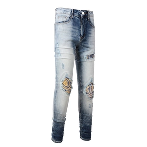 Detail of distressed men's slim denim jeans showing ripped knees with striped fabric patches