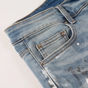 Close-up of light blue graffiti jeans featuring paint splatter details and metal rivets