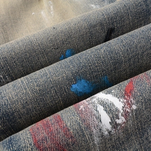 Detailed close-up of blue denim fabric with artistic red and white paint splatter graffiti