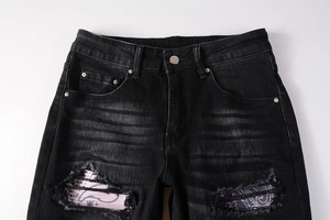 Close-up of distressed black jeans featuring pink paisley patches and cat-whisker washing