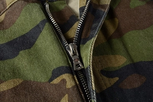 Close-up of durable metal zipper on army green camouflage cargo pants with canvas texture