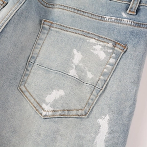 Detail of light blue denim jeans with artistic white paint splatters and stitched pocket