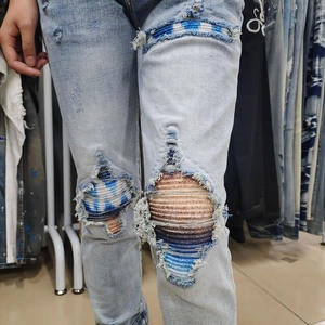 Detail of light blue distressed jeans featuring large rips with colorful striped fabric lining