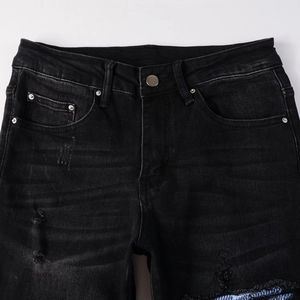 Detailed close-up of men's black distressed jeans with metal button and ripped texture