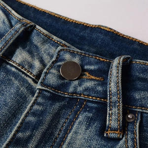 Dettaglio di jeans in denim lavato blu scuro con bottone in metallo e cuciture gialle