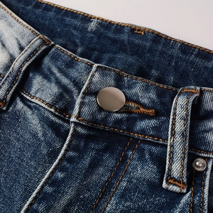 Detail view of washed blue denim waistband with silver metal button and orange stitching