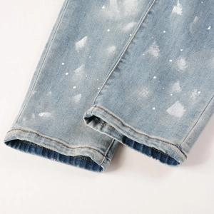 Detailed macro view of light blue denim cuffs with white paint splatters and stitched hem