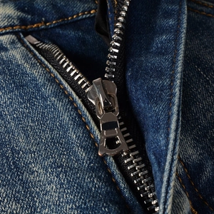 Dettaglio macro della cerniera in metallo e cuciture arancioni sui jeans in denim