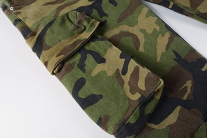 Detailed close-up of side flap pocket on camouflage cargo pants with metal rivet reinforcement