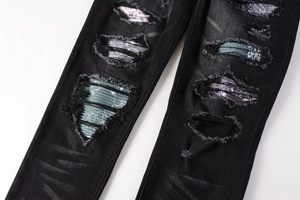 Close-up of black ripped jeans with colorful paisley patches and distressed denim details