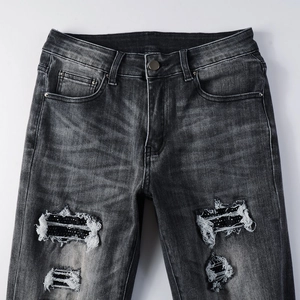 Détail d'un jean gris délavé avec déchirure, paillettes noires et franges blanches stylées