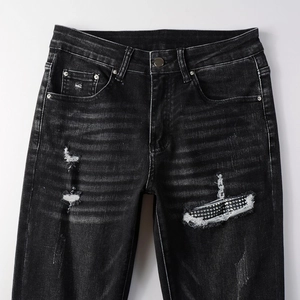 Detail of ripped grey slim fit denim jeans with sparkling rhinestone patch and whiskers
