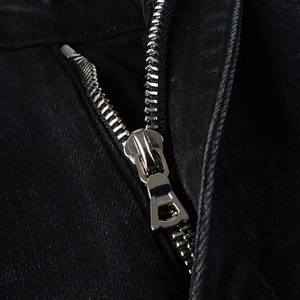 Close-up detail of smooth metal zipper and black denim fabric texture on stylish jeans