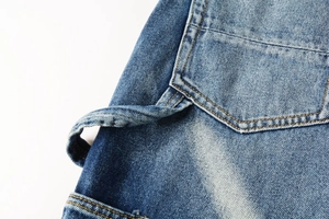 Macro shot of washed blue cargo jeans featuring yellow stitching and fabric strap detail