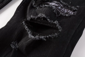 Detailed macro view of distressed black jeans featuring unique snake print patch details
