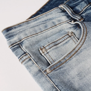 Detail of light blue vintage jeans with orange contrast stitching and silver metal rivets