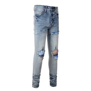 Detail of light blue washed jeans featuring ripped holes with striped knit patches