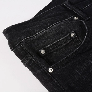 Detail of black slim jeans featuring denim texture and silver metal rivets on the pocket