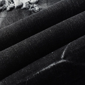 Macro detail of black distressed denim fabric with ripped texture and twill structure