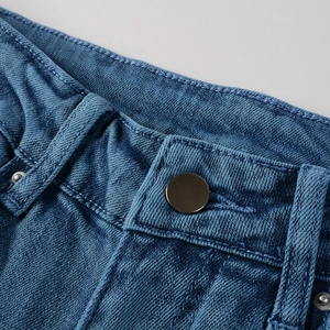 Détail de la taille d'un jean bleu avec bouton en métal bronze et coutures nettes
