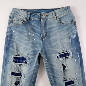 Detail of ripped jeans with blue rhinestone patches and white paint splatter accents
