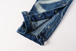 Detail of distressed blue denim hem featuring silver metal snap buttons and orange stitching