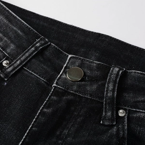 Close-up of black denim jeans featuring metal button, rivets, and faded texture details