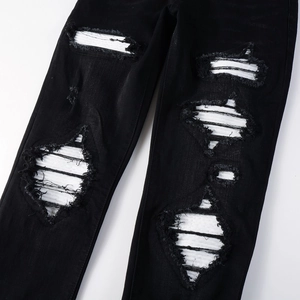 Close-up of black ripped jeans featuring distressed denim and white quilted patch details