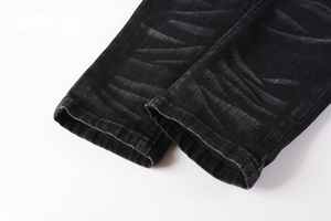 Detailed close-up of washed black denim hem with whiskers and reinforced stitching