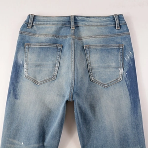 Detail view of light blue washed denim jeans featuring white paint splatter art on back pockets