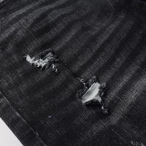 Detailed close-up of distressed black washed denim with ripped holes and white fibers