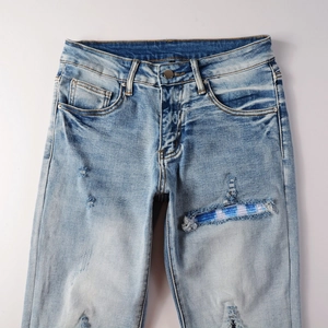 Detail view of men's distressed slim jeans with blue and white plaid patch and ripped denim