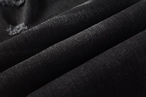 Close-up macro of black distressed denim fabric texture with twill weave and frayed details