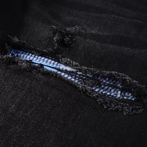 Detail of ripped black denim jeans showing blue and white striped inner fabric lining