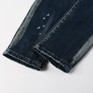 Dettaglio dell'orlo dei jeans blu scuro con schizzi di vernice e cuciture arancioni
