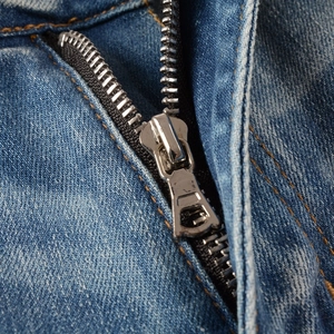 Macro shot of silver metal zipper detail and orange stitching on blue denim jeans