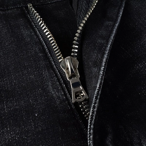 Detailed macro view of silver metal zipper on high-street black distressed denim jeans
