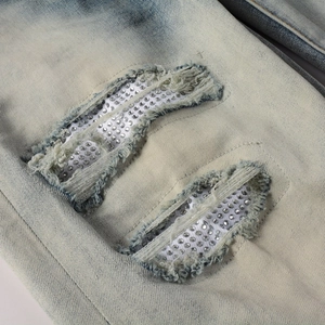 Dettaglio macro di jeans blu da uomo con strappi e decorazioni in strass argentati