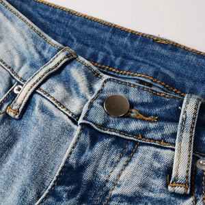 Close-up of blue distressed jeans waist with silver button and orange contrast stitching