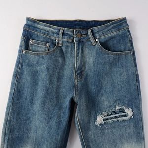 Detail of vintage blue distressed jeans with whiskers and patched ripped elements